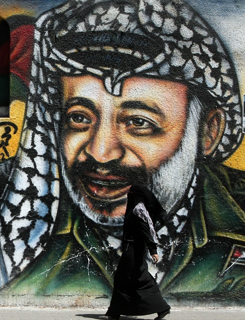 A Palestinian woman walks past a mural of late Palestinian leader Yasser Arafat in Gaza City AFP PHOTO/MAHMUD HAMS