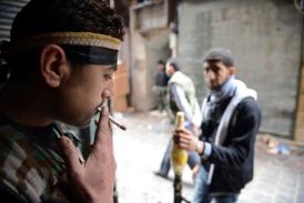 A Syrian rebel smokes a cigarette as his comrade stands guard with an RPG. (AFP / Philippe Desmazes)