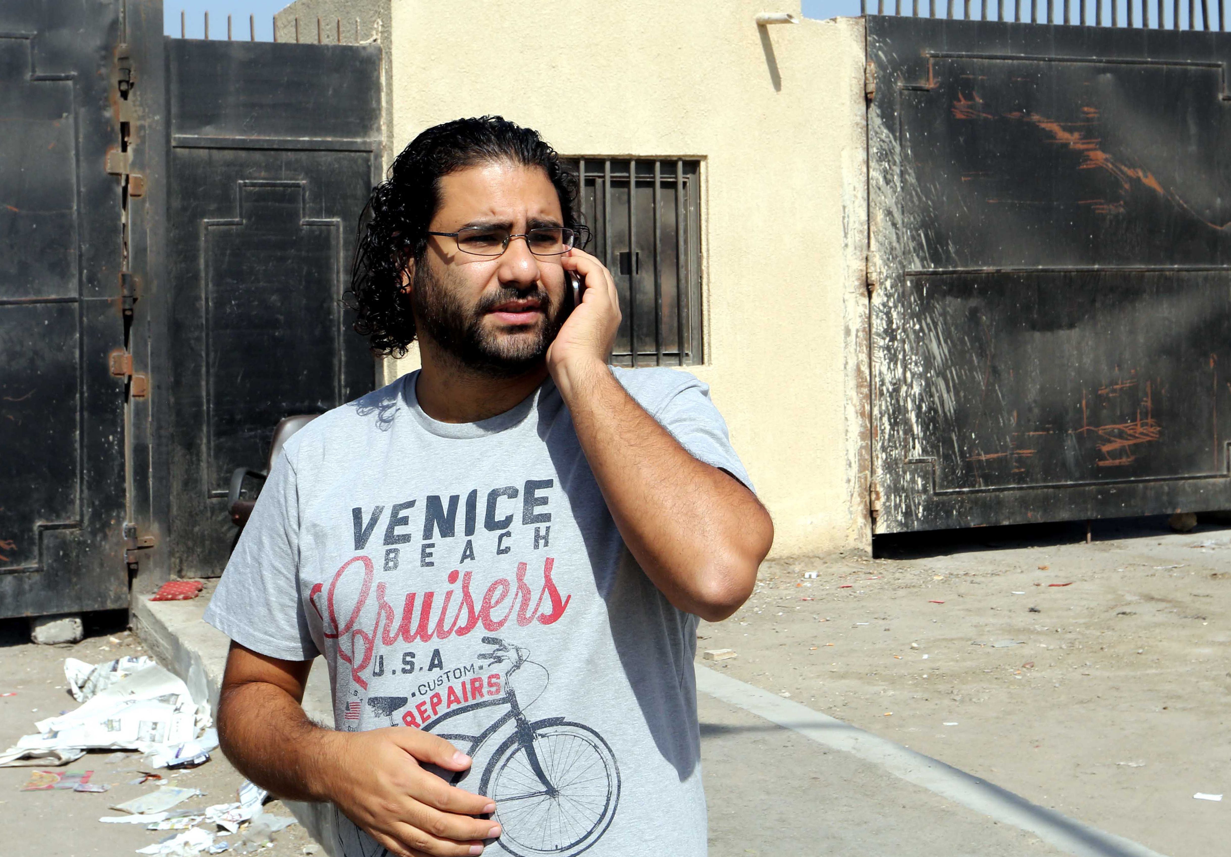 Egyptian prominent activist Alaa Abdel Fattah stands outside the police academy in Cairo's Tora prison after he was denied entrance to attend his trial on June 11, 2014. An Egyptian court sentenced in absentia Fattah to 15 years in jail on charges of participating in an illegal protest, his lawyer told AFP. Twenty-four other activists were also sentenced, in absentia, to 15 years in jail each on the same charges. (AFP PHOTO/STR)