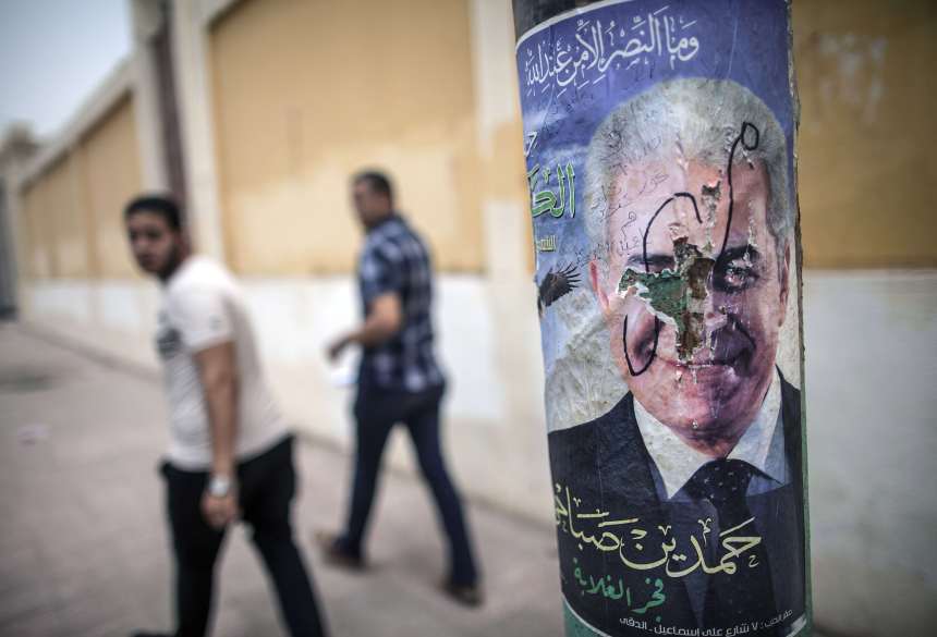Egyptian men sit next to defaced campaign poster of Egypt's Hamdeen Sabbahi, the sole rival to the former army chief expected to romp to victory in next week's presidential election, in Fayyum some 100 kilometres south of Cairo on May 20, 2014. The veteran leftist leader regularly invokes the slogans of "Bread, freedom and social justice" chanted by millions during the uprising that ousted strongman Hosni Mubarak, in campaigning across the country for the May 26-27 poll. (AFP PHOTO / MAHMOUD KHALED)