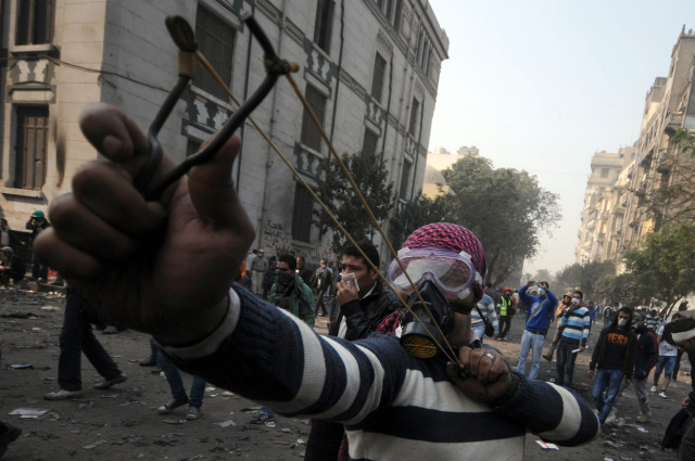 An Egyptian youth wearing a gas mask aims a slingshot during clashes in Cairo, on 22 November, 2011 (AFP/file photo)