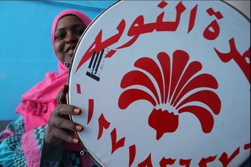 A woman upholds a drum with a Nubian logo (Photo by Aurora Ellis)